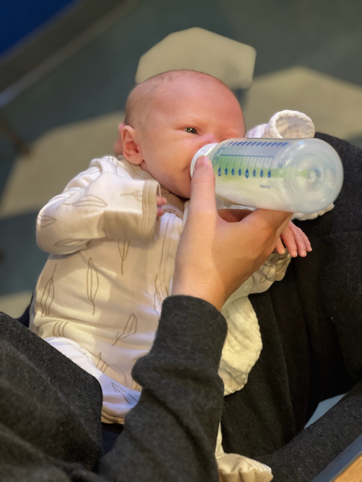 A newborn feeding from a bottle while held upright